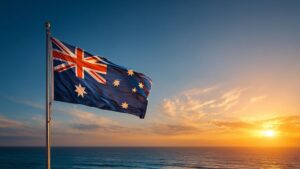 Australian flag flying on a flagpole against a coastal sunset sky, with the ocean visible in the background.